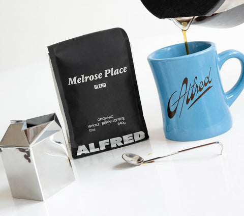 Coffee bag labeled 'Melrose Place Blend' and a blue mug with 'ALFRED' branding on a white surface.